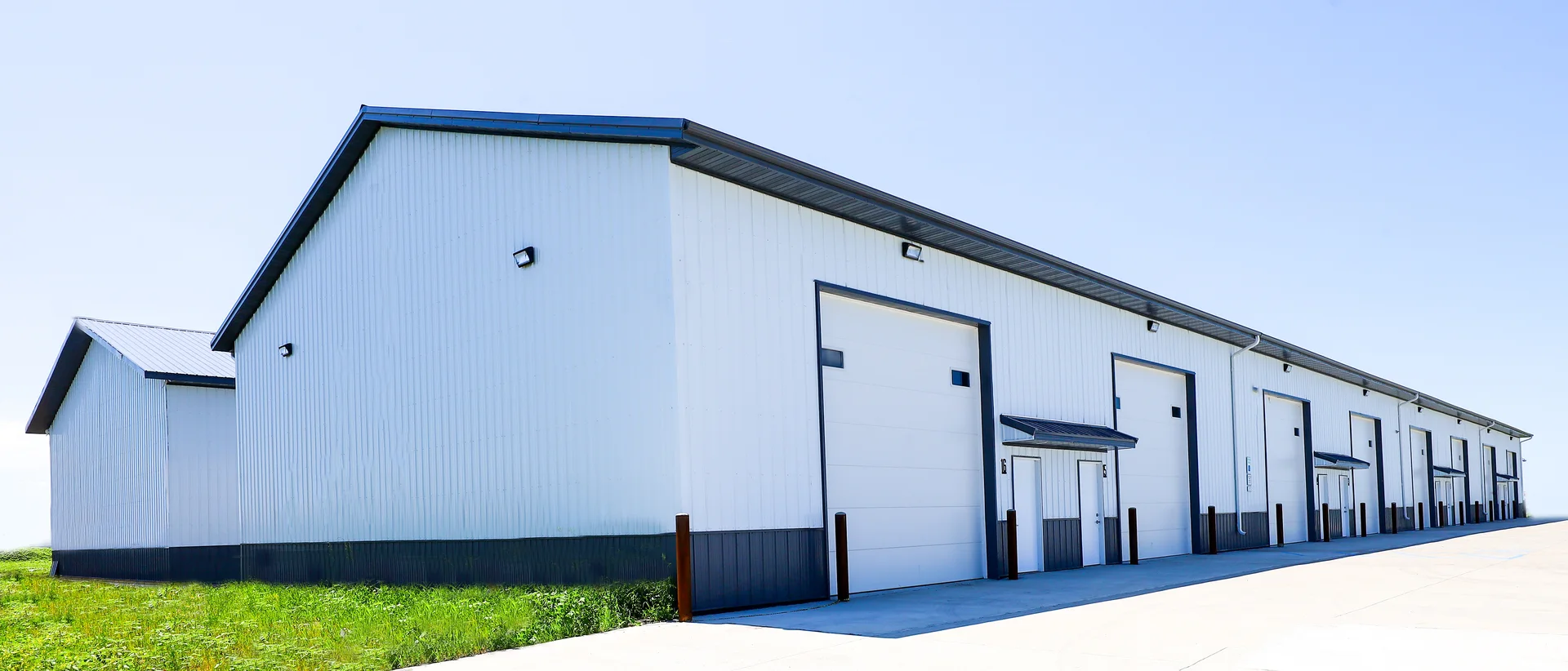 Long post-frame shop building with light-colored metal siding and multiple overhead doors